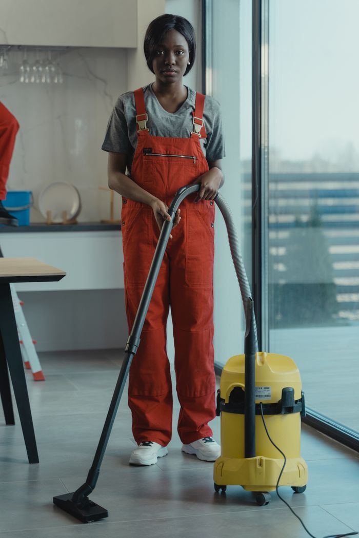 Une femme adulte en combinaison rouge utilise un aspirateur dans un intérieur moderne, en se concentrant sur les tâches de nettoyage.